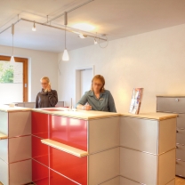 Der großzügige Empfangstresen von USM Haller wurde mehrfarbig gestaltet. Grau und Rot harmonieren perfekt mit den auf Maß gefertigten Holz-Abdeckplatten. Der großzügige Empfangstresen von USM Haller wurde mehrfarbig gestaltet. Grau und Rot harmonieren perfekt mit den auf Maß gefertigten Holz-Abdeckplatten.
