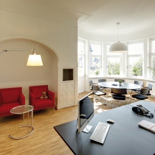 In den hohen, lichtdurchfluteten Raum wurden neben dem Arbeitsplatz mit Büromöbeln von Vitra ein Konferenztisch mit acht Stühlen und eine kleine Sitzecke mit roten Ledersesseln integriert. Die Deckenleuchte Skygarden über dem Konferenztisch und die Stehleuchte Tolomeo Mega in der Sitzecke setzen den Raum in das richtige Licht.